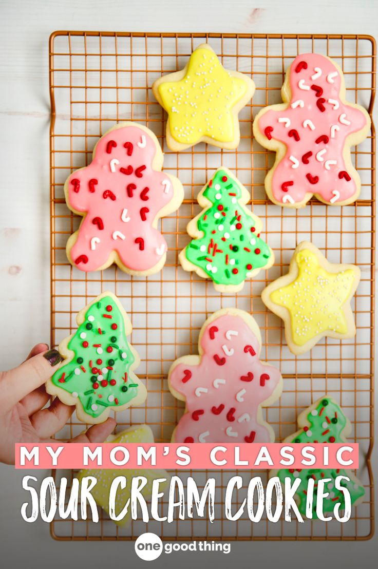 someone is decorating christmas cookies with icing and sprinkles on a cooling rack