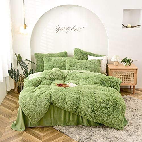 a bed with green comforter and pillows in a room next to a plant on the floor