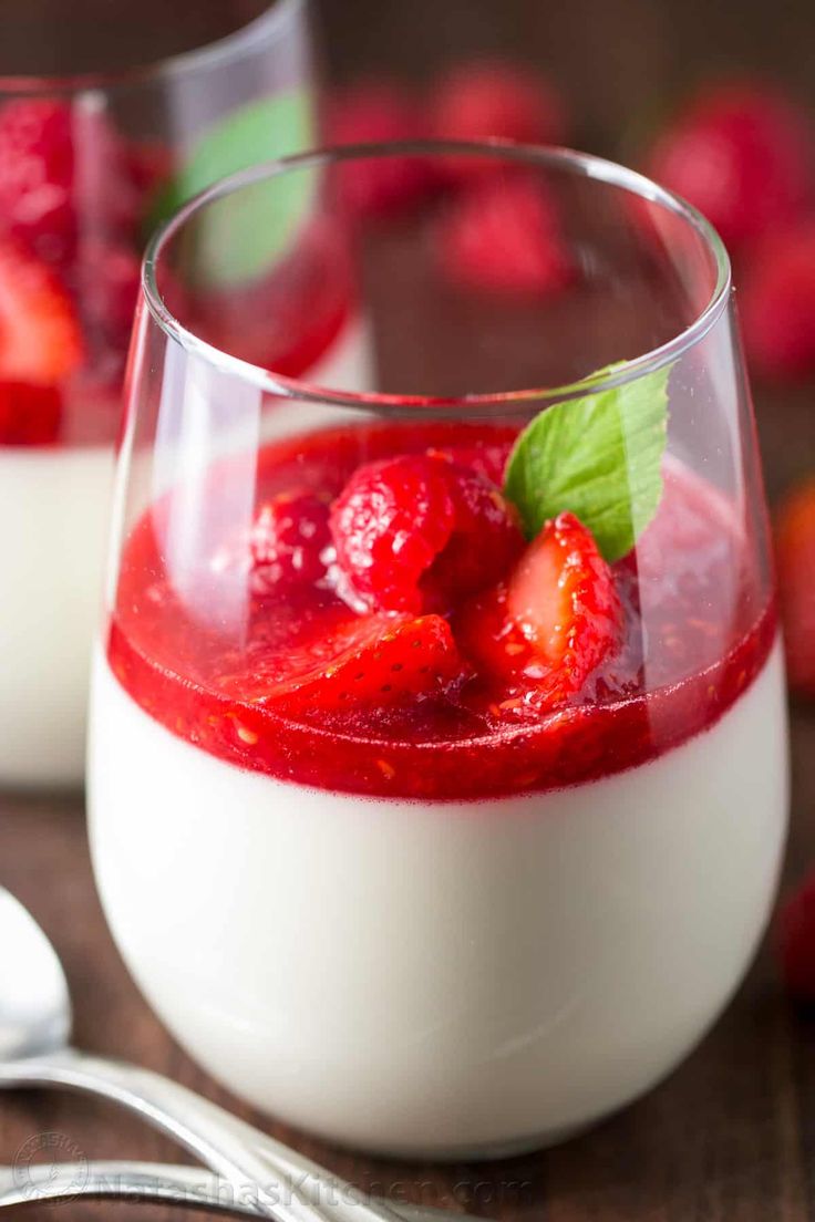 two glasses filled with yogurt and strawberries next to some raspberries