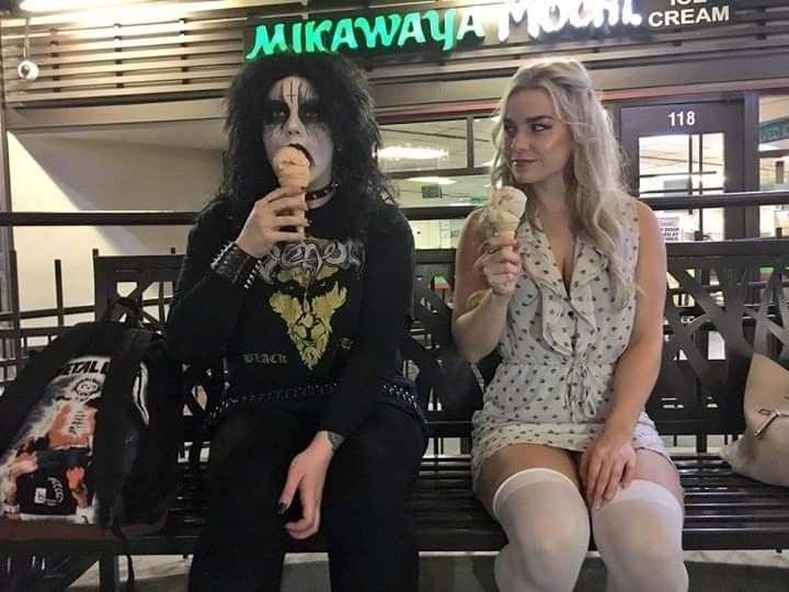 two women are sitting on a bench eating ice cream and one is dressed as michael jackson