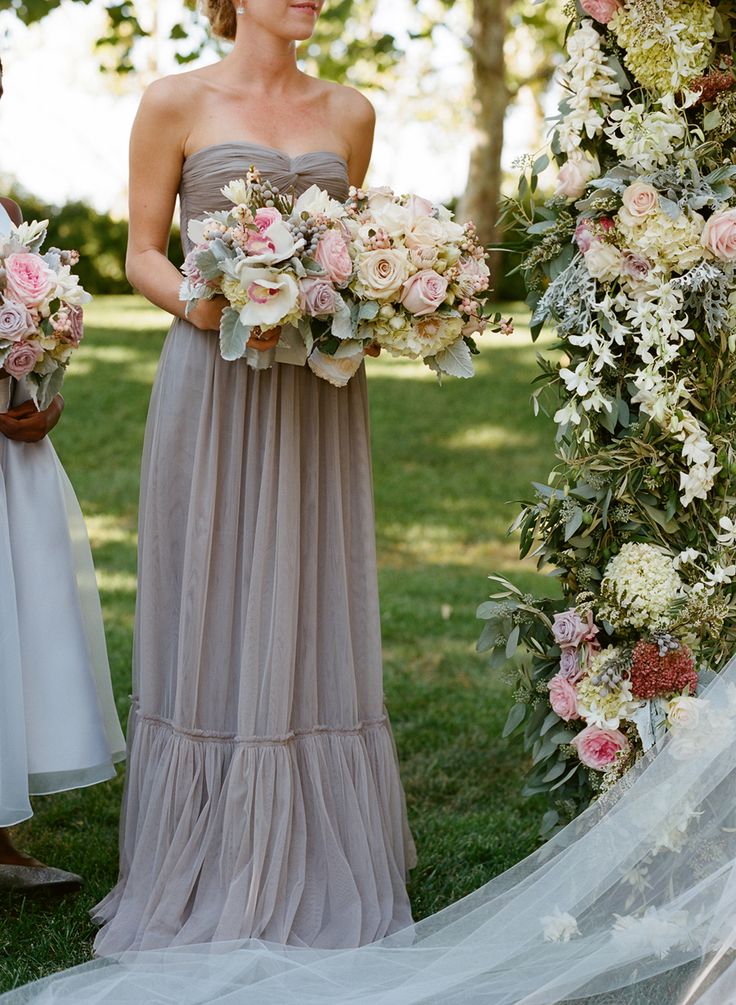 two women standing next to each other in front of a flower covered arch with flowers on it