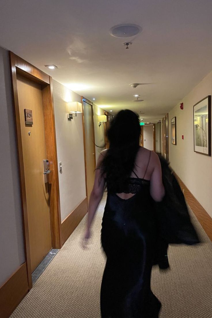 a woman in a black dress walking down a hallway