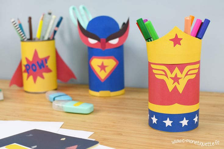 some pencils and markers are sitting on a table with superhero themed pens in them