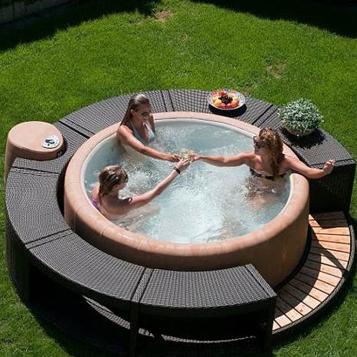 three people in an outdoor hot tub on the grass with two children playing around it