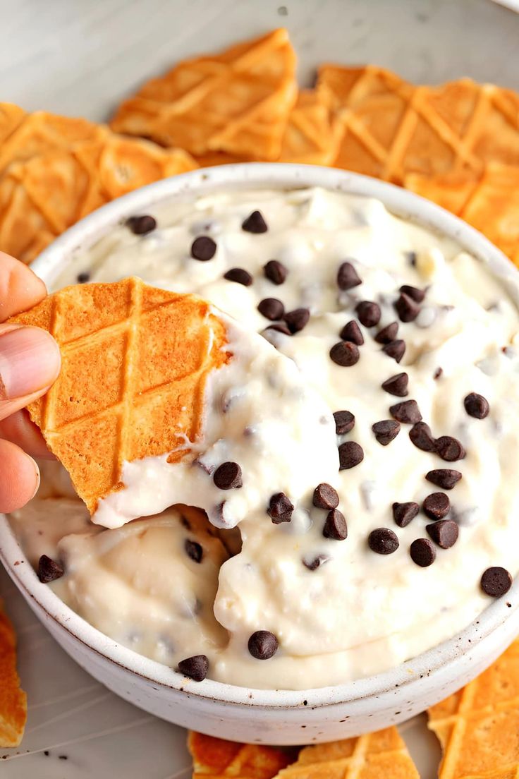 a hand holding a cracker over a bowl of ice cream and chocolate chips