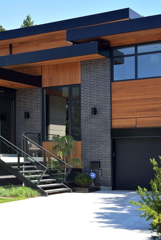 a modern house with wood siding and black metal railings on the front door, stairs leading up to the second floor