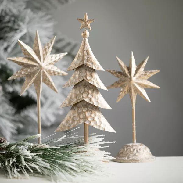 three small wooden christmas trees on top of a white table next to a pine tree