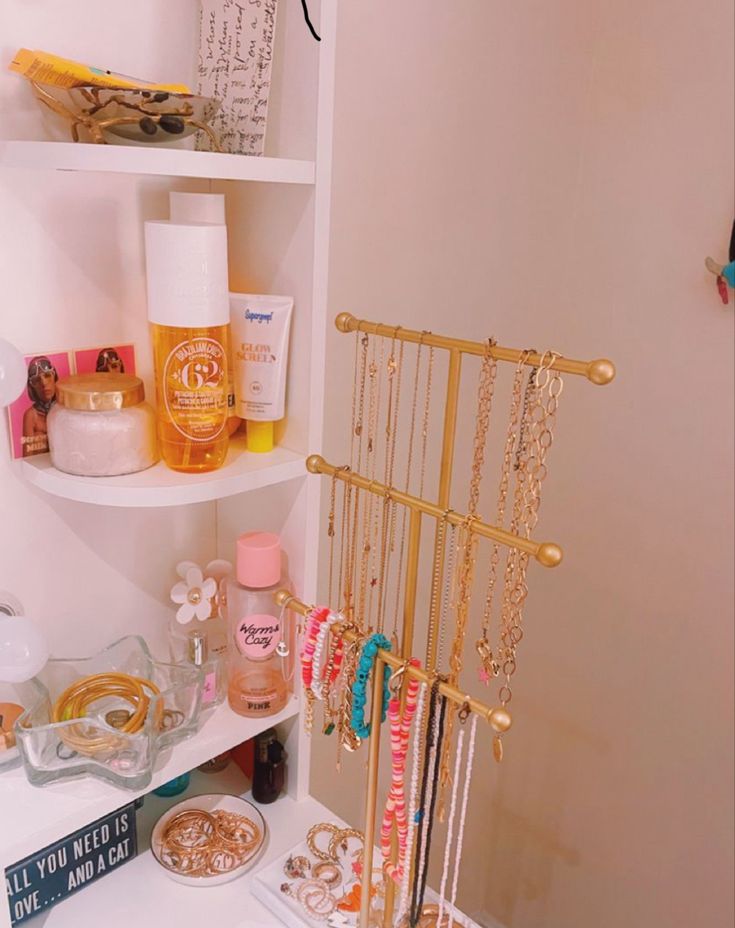 there is a shelf with many items on it in the bathroom that includes necklaces, bracelets and other personal care products