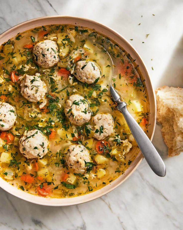 a bowl filled with meatballs and vegetables next to a piece of bread on a table