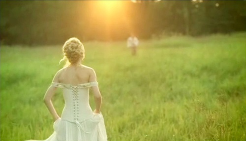 a woman in a wedding dress standing in a field with her back to the camera