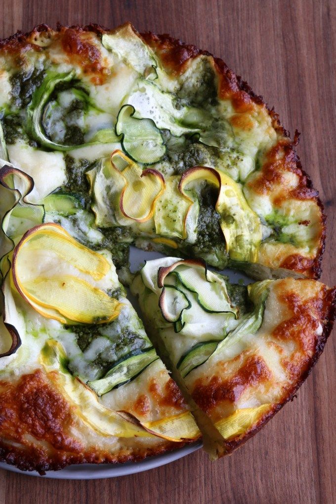 a pizza with zucchini, cheese and other toppings on a wooden table