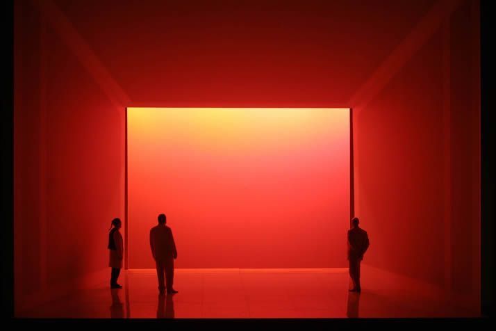 three people standing in an empty room with red light coming from the ceiling and floor