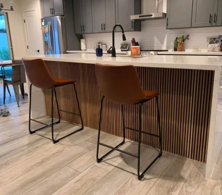 two bar stools sitting in front of a kitchen island with wooden slats on it