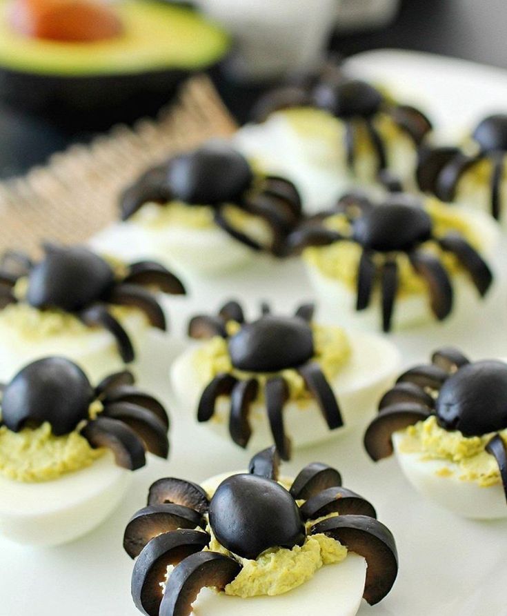 deviled eggs decorated with black spider legs on a white platter, ready to be eaten