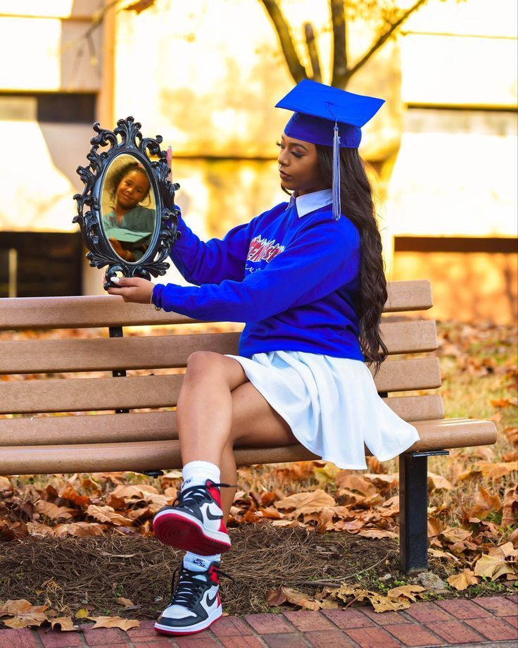 a woman in a graduation cap and gown sitting on a bench holding a small mirror