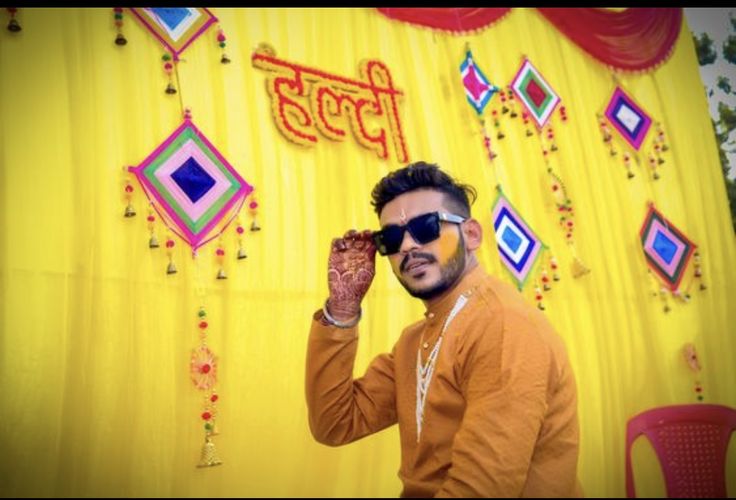 a man in an orange shirt and sunglasses standing next to a wall with decorations on it