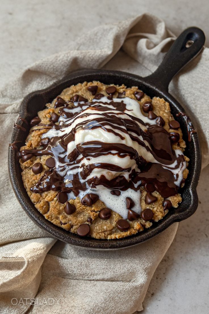 a skillet filled with chocolate chip cookies covered in cream and drizzled