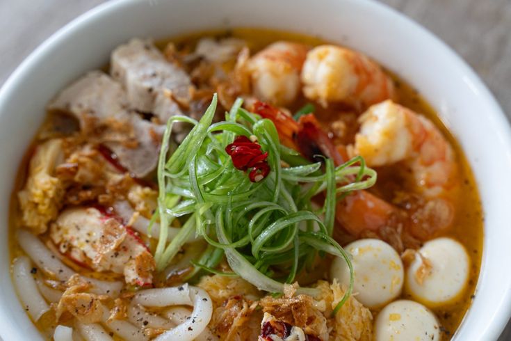 a white bowl filled with shrimp, noodles and other foods on top of a table