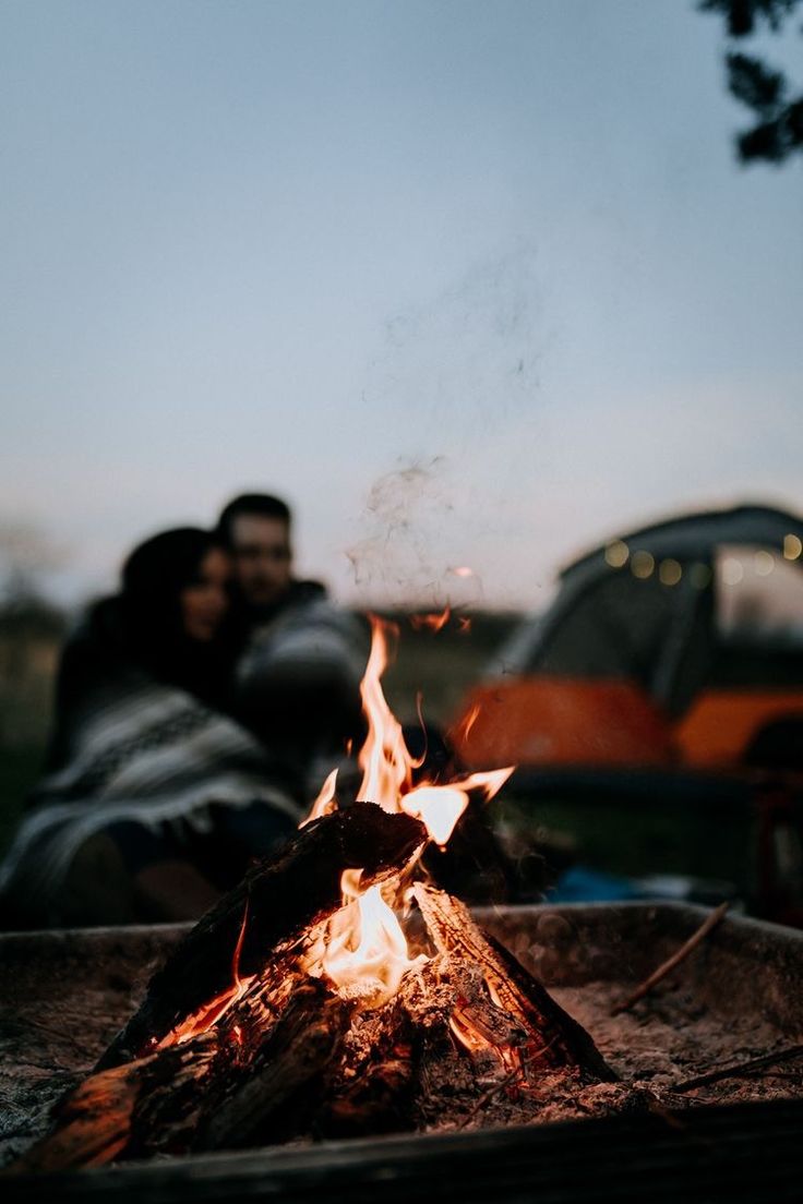 a man and woman sitting next to a campfire