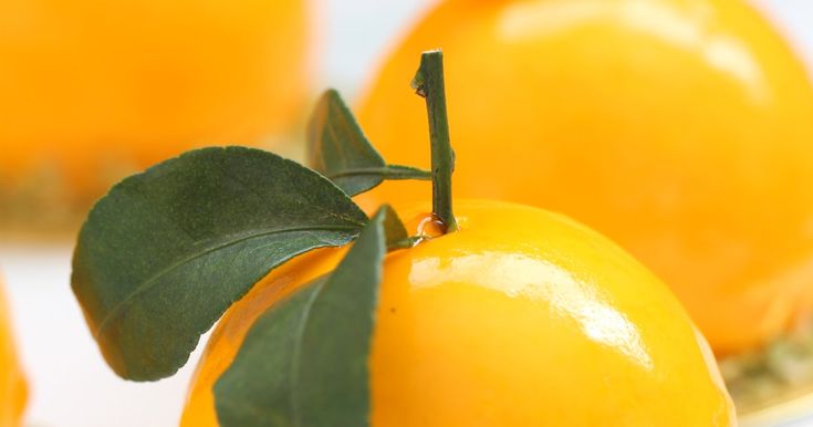 three oranges with green leaves on them sitting in front of some other oranges