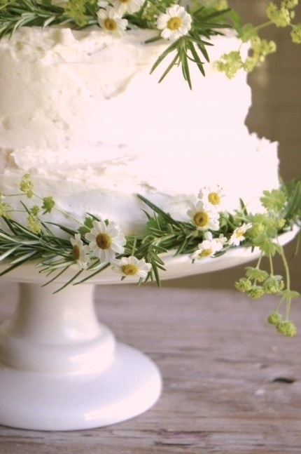 a white cake with flowers and greenery on top is sitting on a wooden table