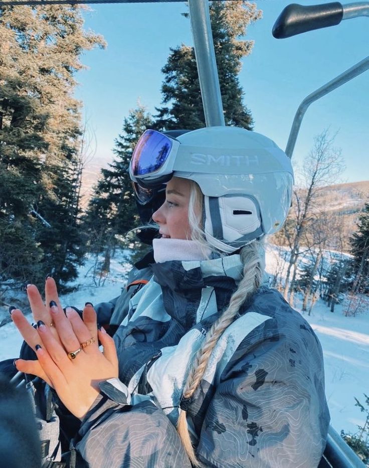 a woman sitting on a ski lift holding her hand up to the side with trees in the background