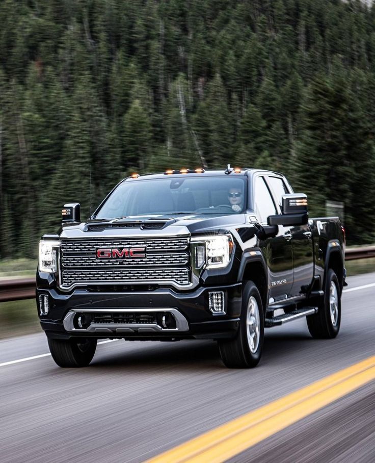 a black truck is driving down the road with trees in the backgrouund