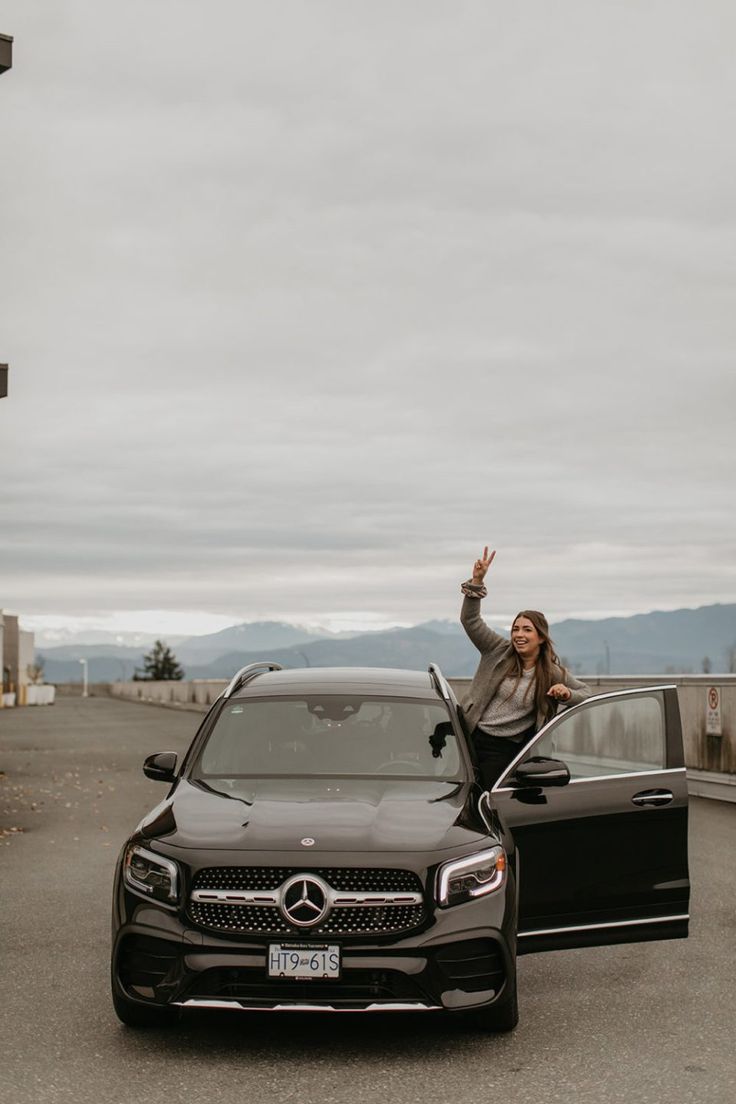 a woman standing next to a black mercedes benz s - class in front of a car