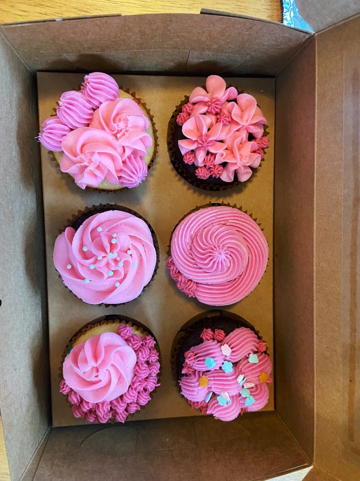 six cupcakes in a box with pink frosting and flowers on the top