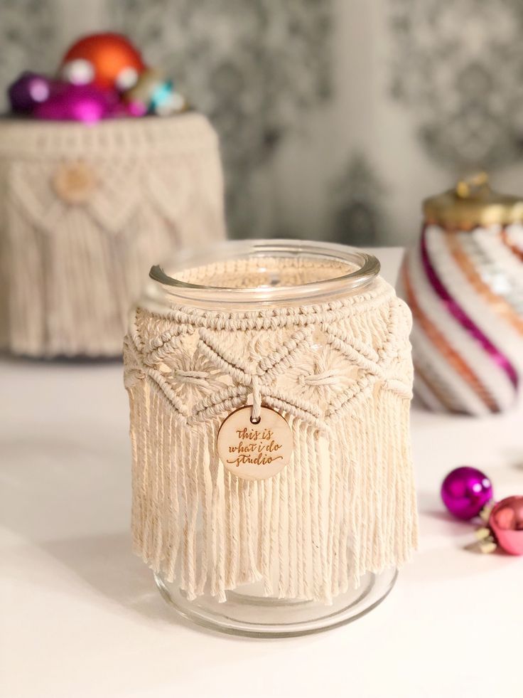 a glass jar with tassels and ornaments around it on a white countertop