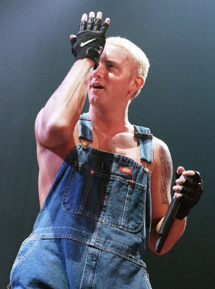 a man in overalls holding a microphone up to his ear while performing on stage