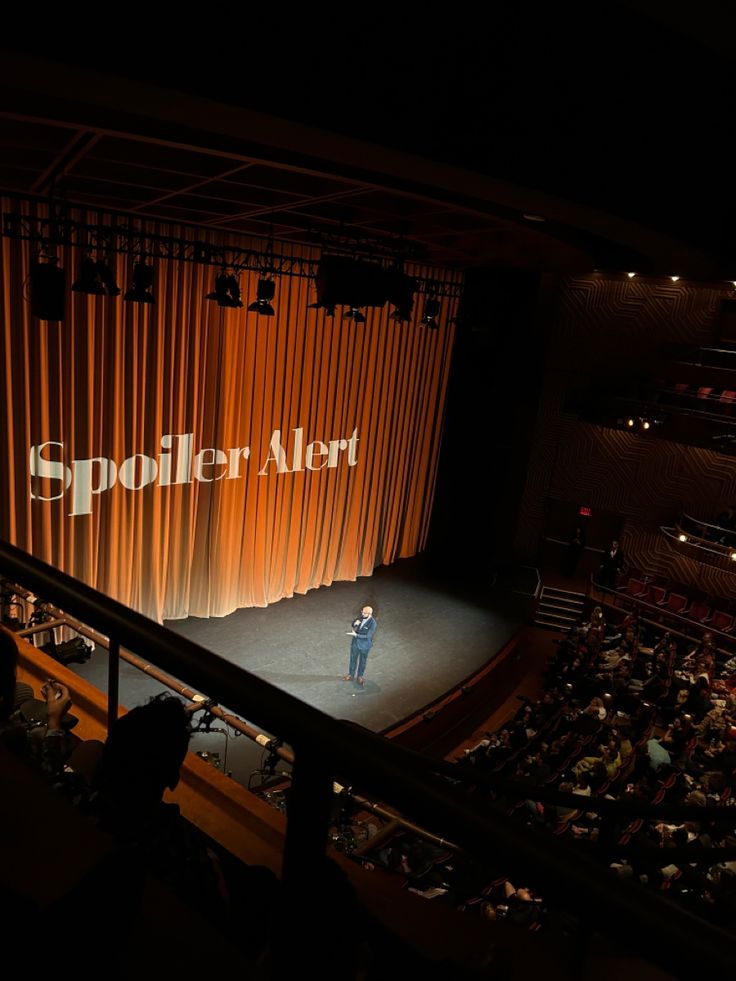 a man standing on top of a stage in front of an auditorium filled with people