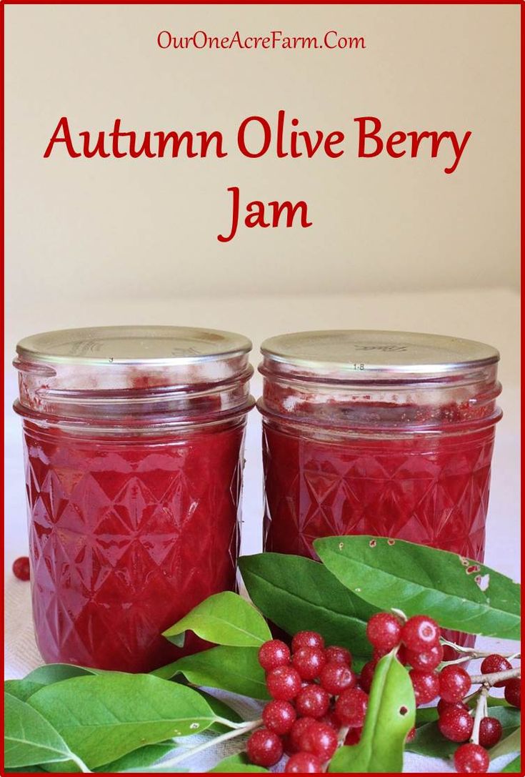 two jars filled with jam sitting on top of a table next to leaves and berries