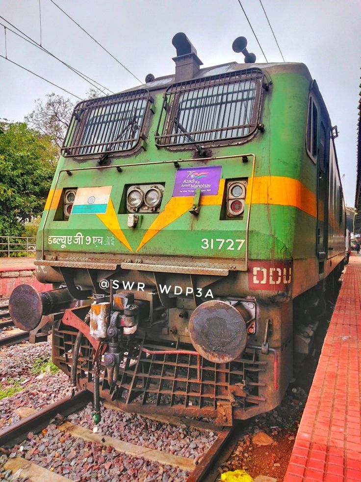 an old green train is parked on the tracks near some brick walkways and trees