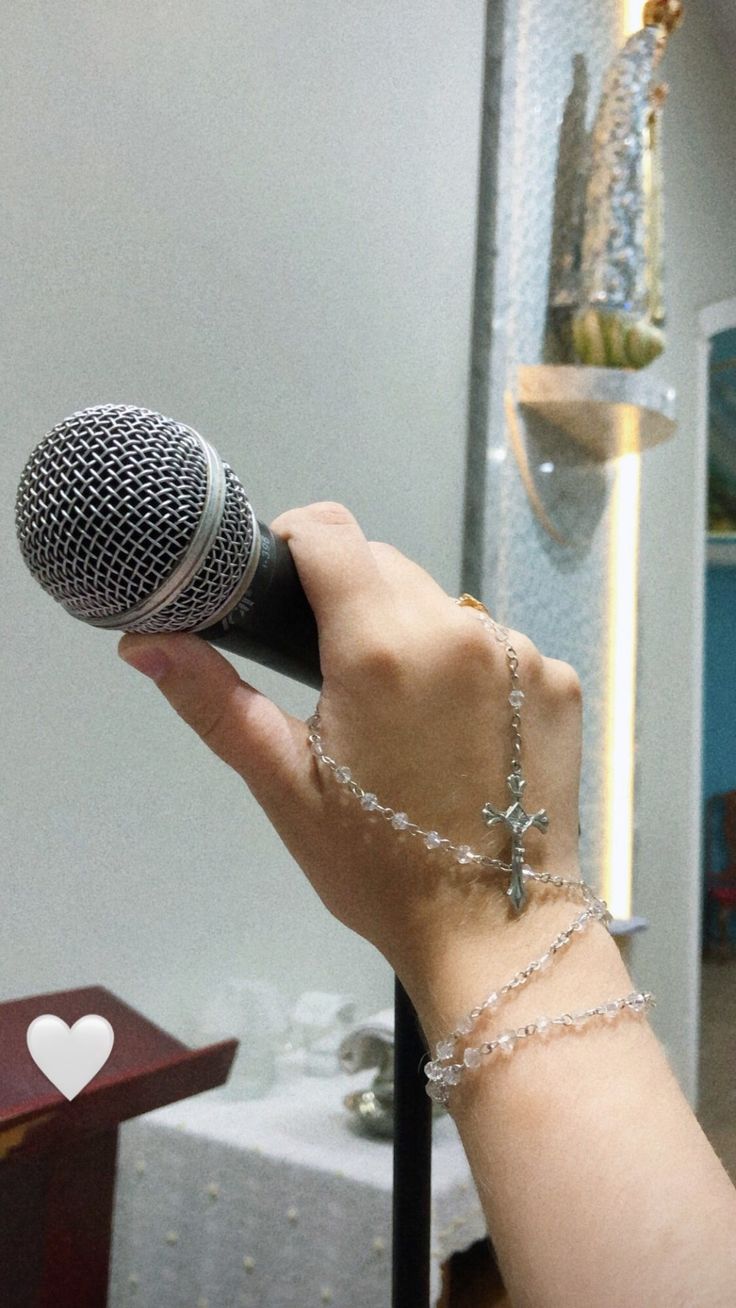 a person holding a microphone in their hand with a chain on the wrist and a heart hanging from it