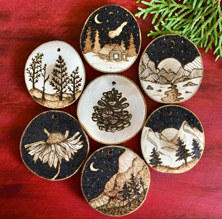 six hand painted ceramic ornaments on a wooden surface with pine tree and cabin in the background