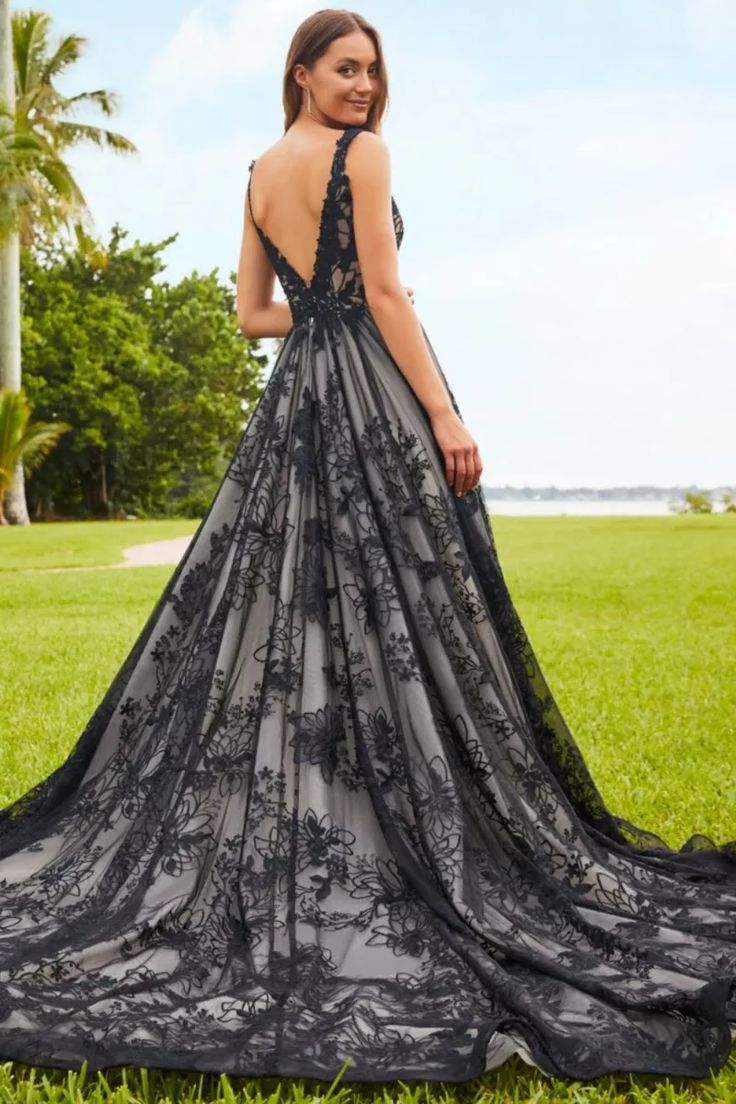 a woman standing in the grass wearing a black dress with floral lace on it and open back