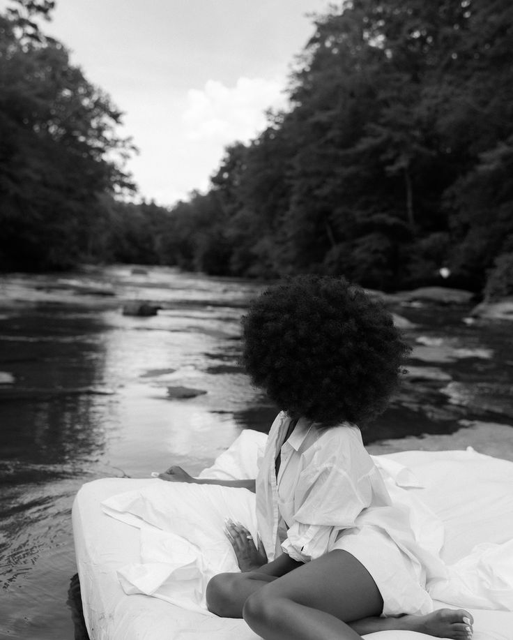 a black and white photo of a woman sitting on a raft in the water with trees behind her