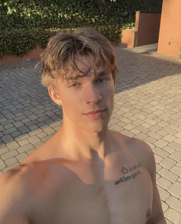 a shirtless young man standing in front of a brick walkway