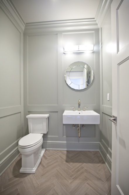 a white toilet sitting next to a sink in a bathroom under a round mirror on the wall