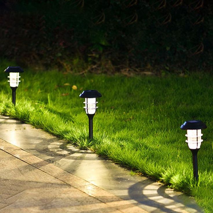 four lawn lights are lined up on the side of a sidewalk in front of some grass