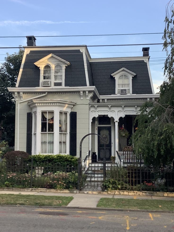 a white house with black shutters on the front and side windows is next to a street