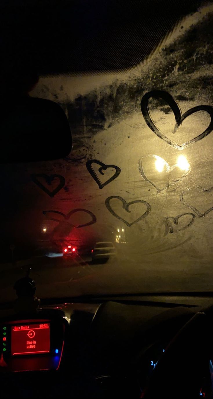 the inside of a car with hearts drawn on it's windshield and lights shining in the background