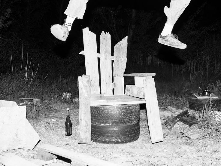 a black and white photo of a person jumping on a skateboard over a chair