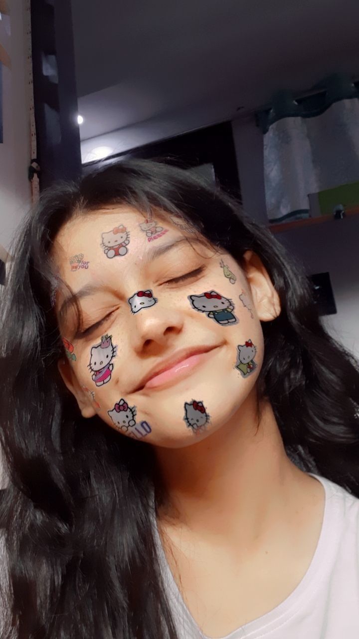 a girl with her face covered in stickers on her face and the words hello kitty painted on her cheek