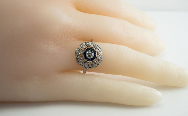 Art Deco Ring, Genuine Diamond Ring, Genuine Sapphire Ring, September Birthstone, Vintage Ring, 14K White Gold Ring, Engagement Ring, Wedding Ring, Elegant Ring. This pretty vintage estate ring is crafted in solid 14K White Gold (carefully tested and guaranteed). The center round brilliant cut diamond is .20 carat. 8 surrounding diamonds total .24 carat. And 24 small diamonds total .24 carat. The total diamond weight is .68 carats. They range from VS2 to SI2 clarity and H color. 14 French cut ab Art Deco Halo Ring With Round Cut, Antique Platinum Cluster Ring, Art Deco Diamond Wedding Ring With Halo Setting, Victorian Style Diamond White Round Cut Diamond Ring, Art Deco Diamond Halo Ring With Round Cut, Art Deco Halo Ring With Brilliant Cut, Art Deco Style Cubic Zirconia Diamond Ring, Sapphire Ring With Single Cut Diamonds, Art Deco 14k Gold Diamond Ring With Halo Setting