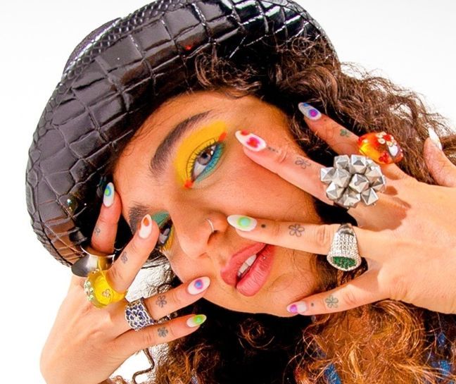 a woman with her hands on her face covered in colorful nail polish and rings, posing for the camera