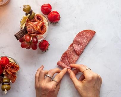 a person cutting up meat on top of a counter next to other food items and fruit