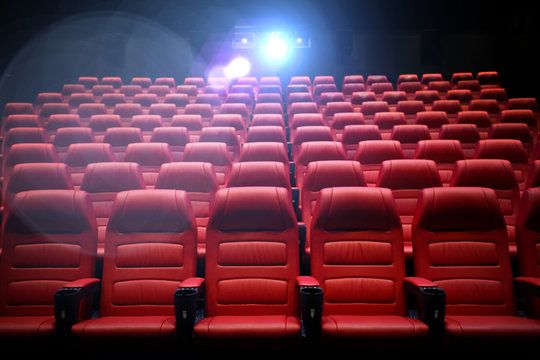 an empty theater with red seats and a projector light