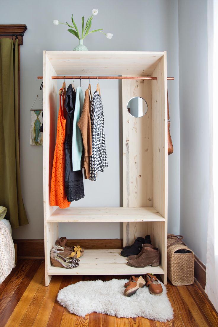 a wooden shelf with shoes and clothes hanging on it in front of a window, next to a white rug